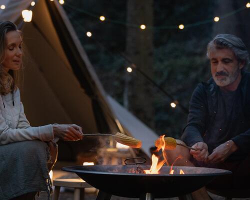 kobieta i mężczyzna spędzający czas przy palenisku obok namiotu