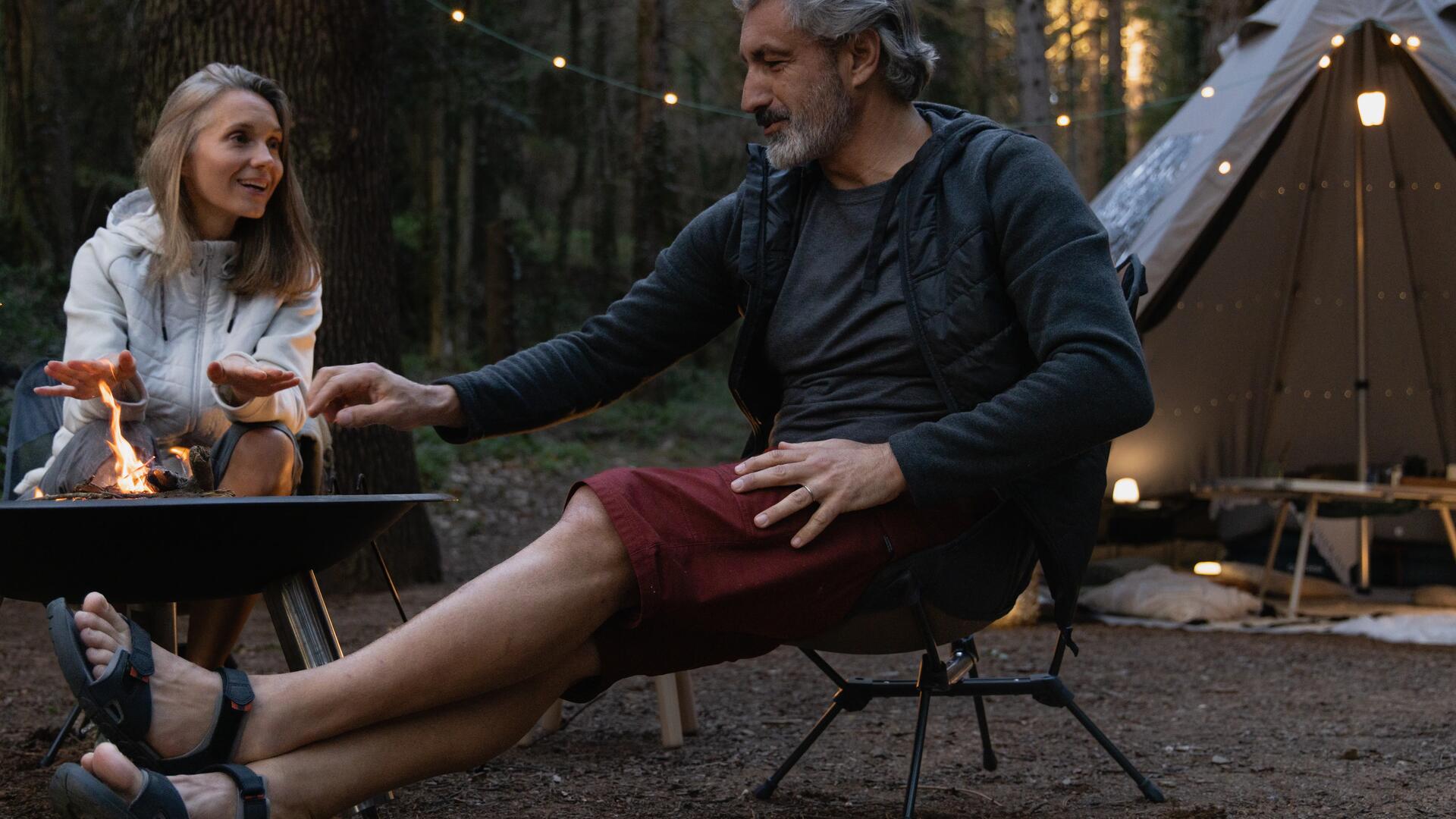mężczyzna i kobieta siedzący przy stoliku turystycznym przed namiotem w lesie