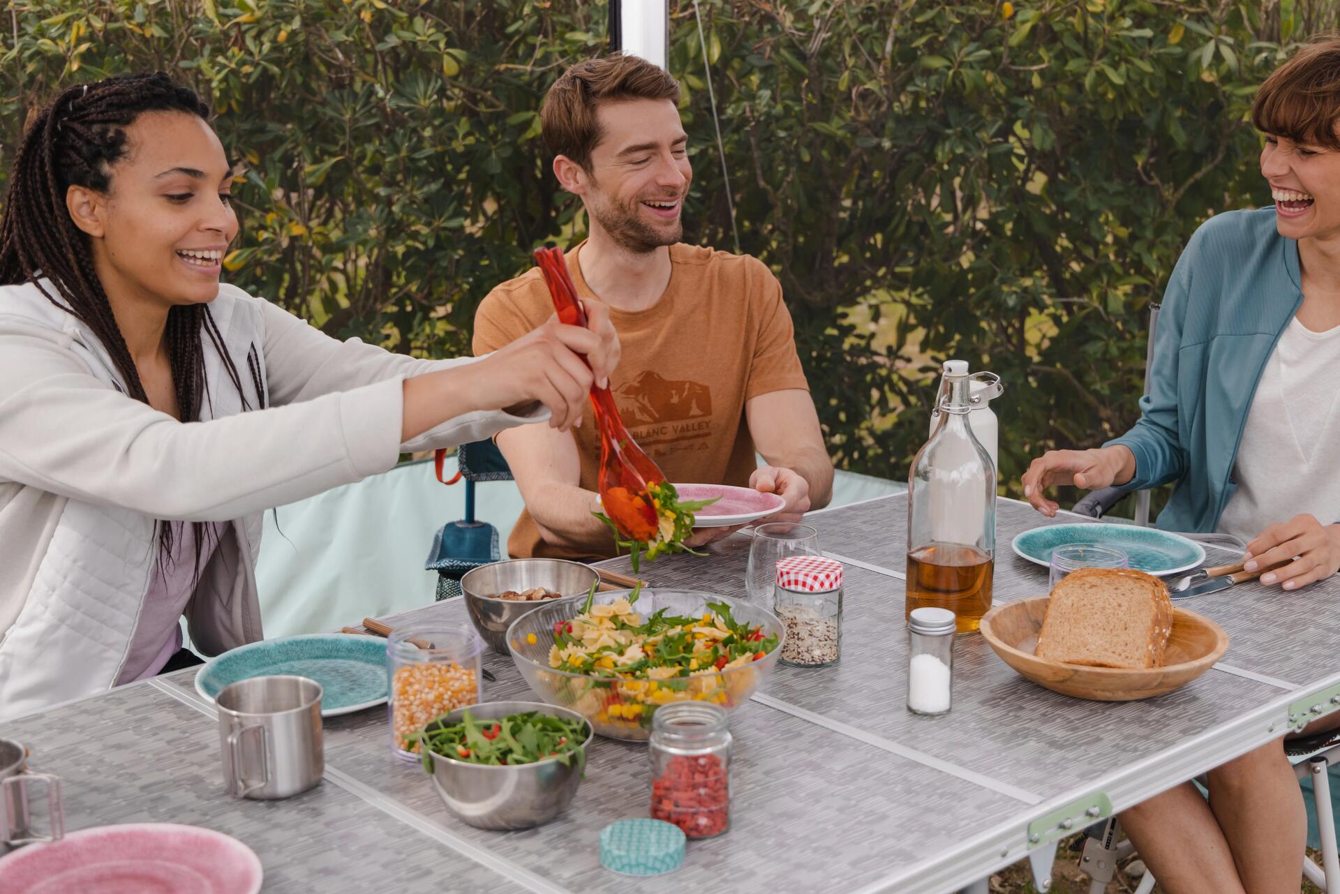 Grupa osób jedzących wspólnie sałatkę z pomidorem ogórkiem i makaronem na stole turytycznym