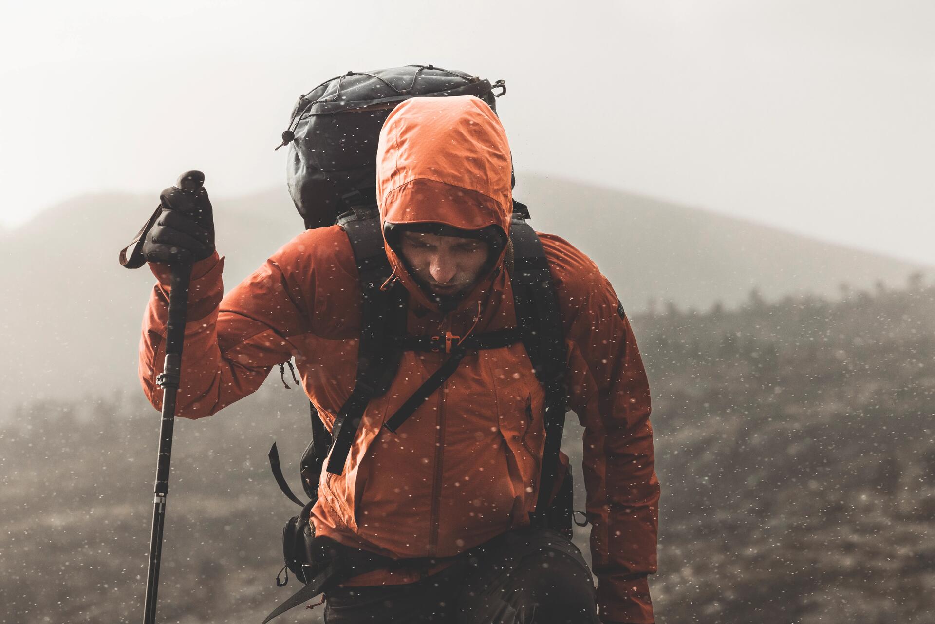 Mężczyzna stojący w górach w nieprzemakalnej kurtce trekkingowej podczas deszczu