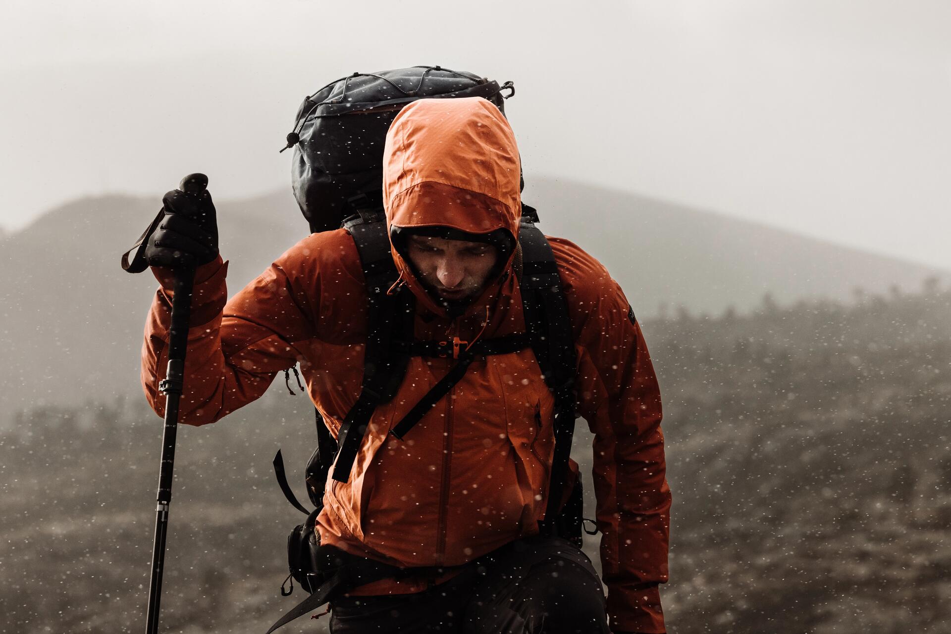 Mężczyzna stojący w górach w nieprzemakalnej kurtce trekkingowej podczas deszczu