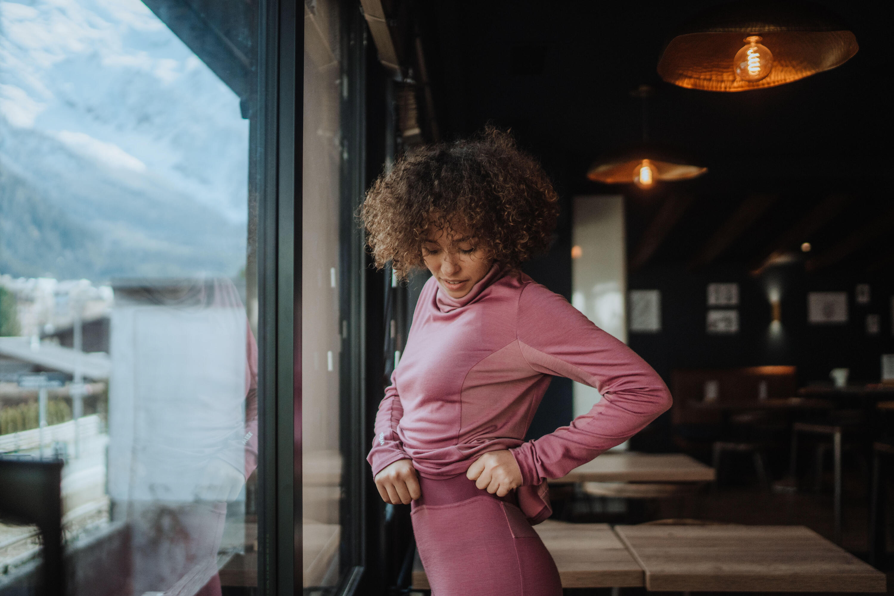 Eine Frau in pinker Baselayer steht vor dem Fenster.