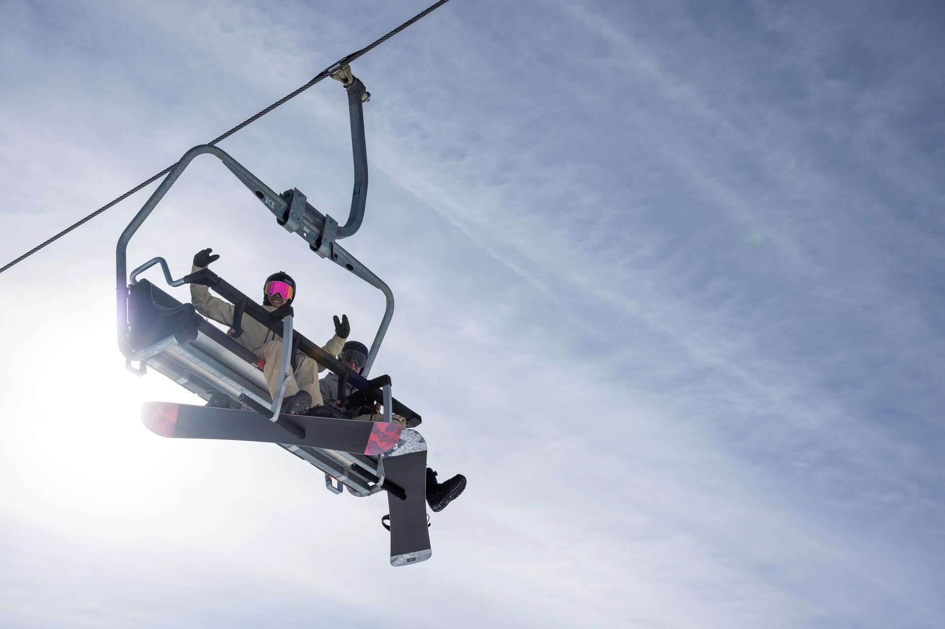 Para z deskami snowboardowymi jadąca wyciągiem krzesełkowym na stok