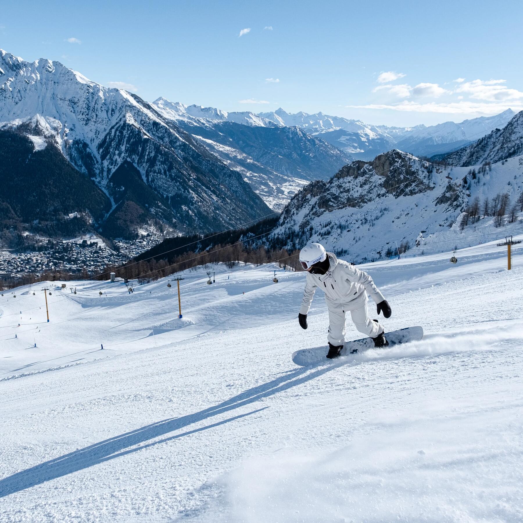 Osoba w odzieży i kasku snowboardowym jadąca ze stoku na desce snowboardowej