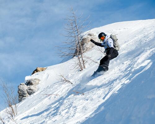 chłopiec w kasku i goglach snowboardowych zjeżdżający na desce snowboardowej ze stoku