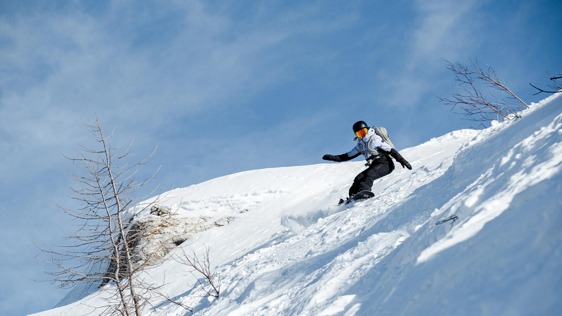 Osoba w odzieży zimowej w kasku i w goglach jadąca na snowboardzie
