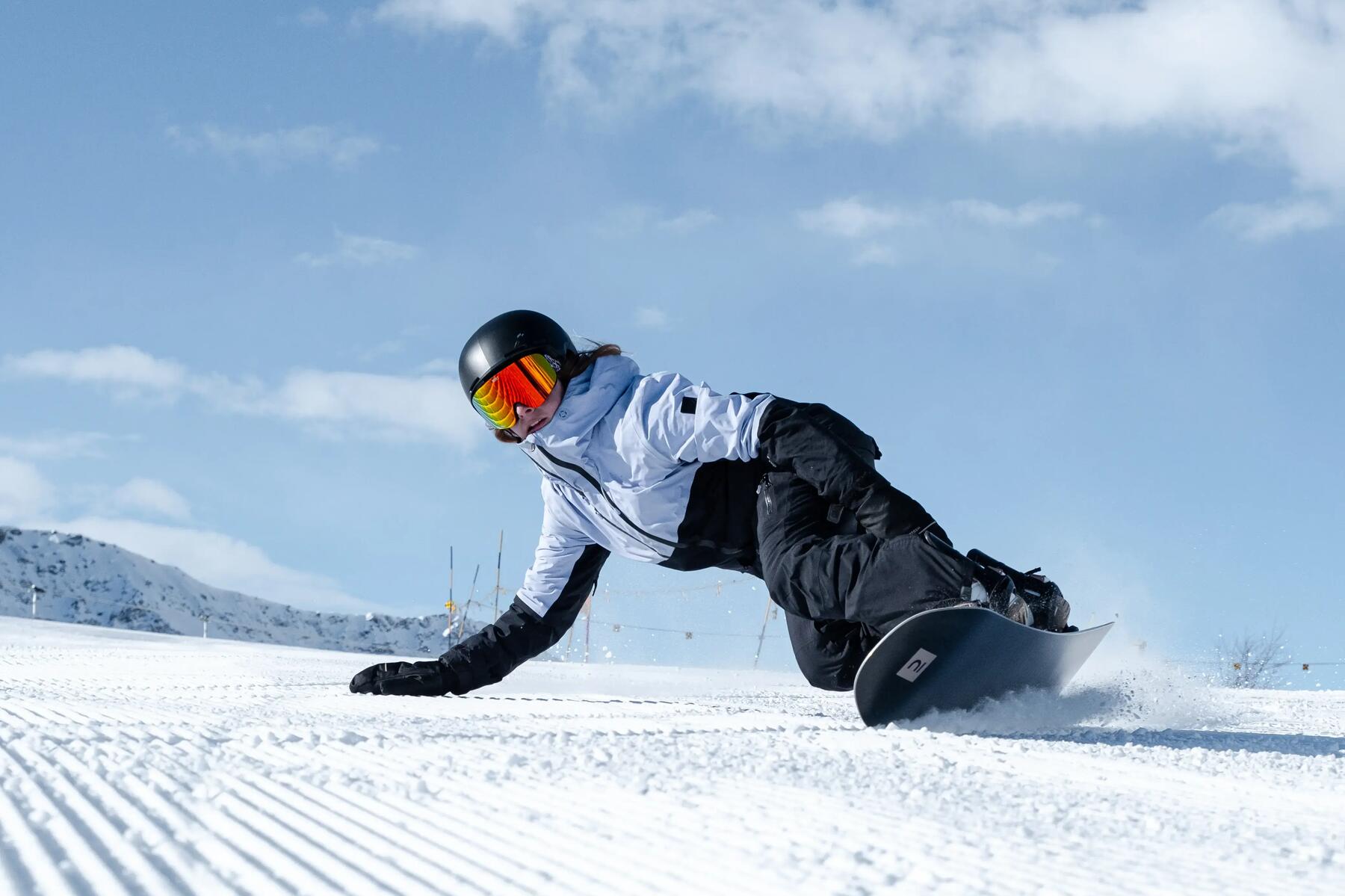 Kobieta na desce snowboardowej w kurtce goglach kasku i rękawicach