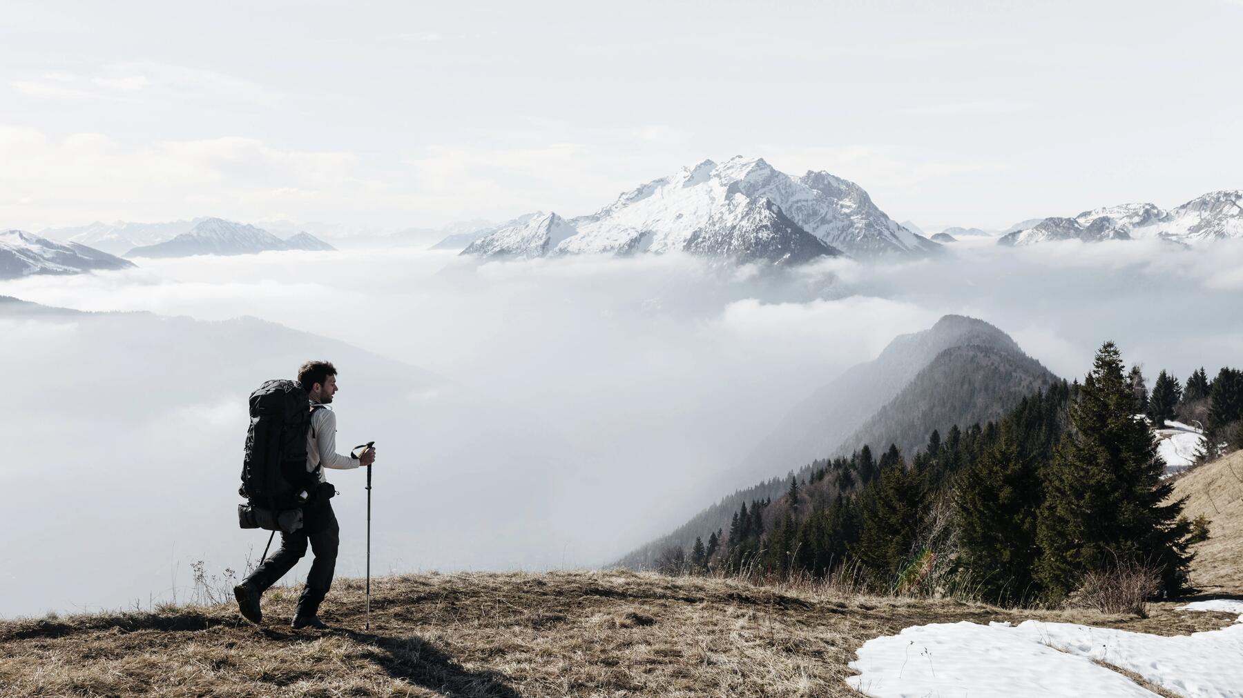 Mężczyzna z plecakaiem trekkingowym i kijkami trekkingowymi w rękach wędrujący po górach 