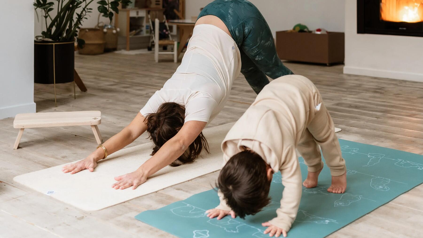 Mutter mit Kind auf zwei Yogamatten bei der Durchführung des herabschauenden Hundes.