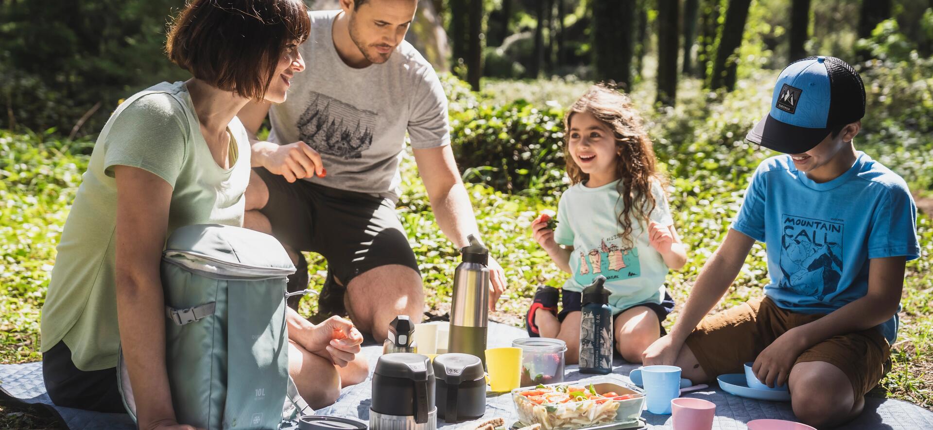rodzina siedząca na pikniku z termosami i naczyniami turystycznymi w lesie
