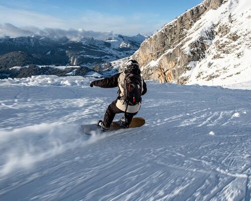 Mężczyzna w odzieży snowboardoej jadący ze stoku na desce snowboardowej dobranej do wzrostu i wagi 