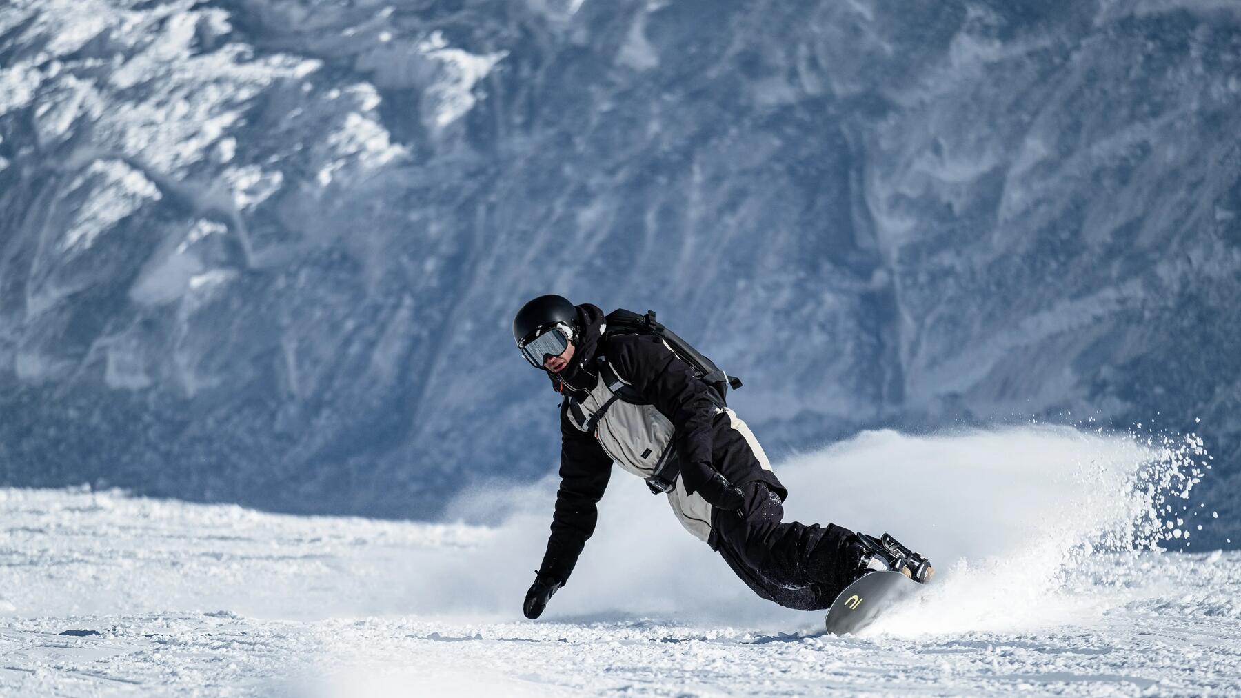 Mężczyzna w odzieży zimowej w kasku i w goglach jeżdżący na snowboardzie