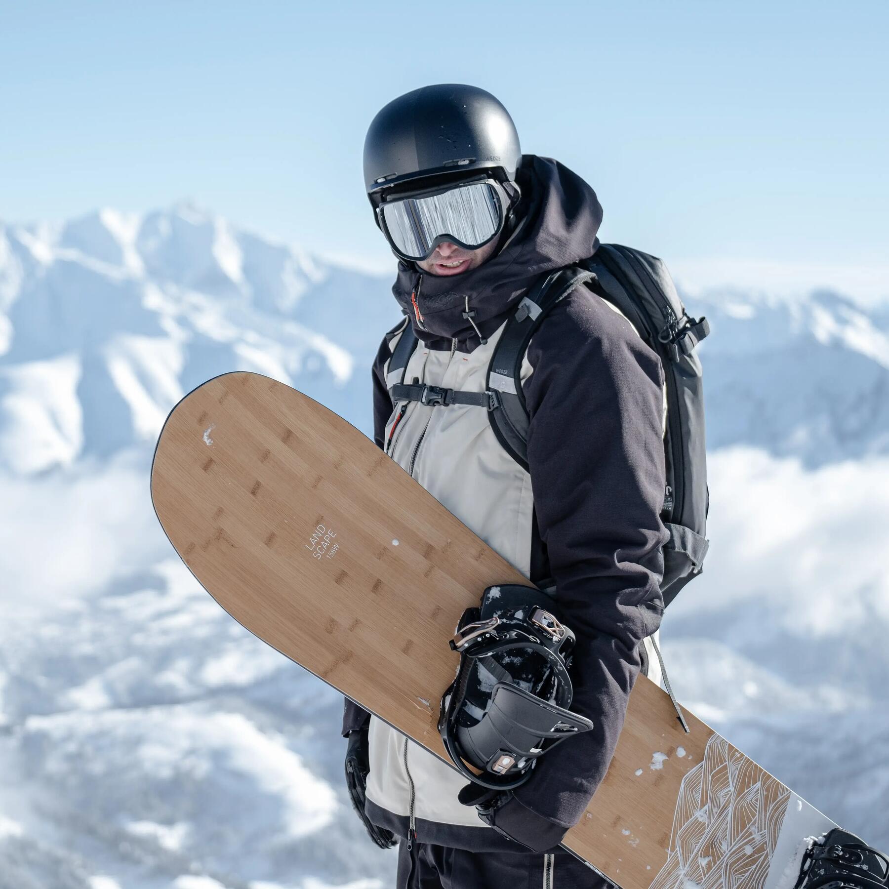 Mężczyzna w kasku i goglach snowboardowych trzymający deskę snowboardową w ręce