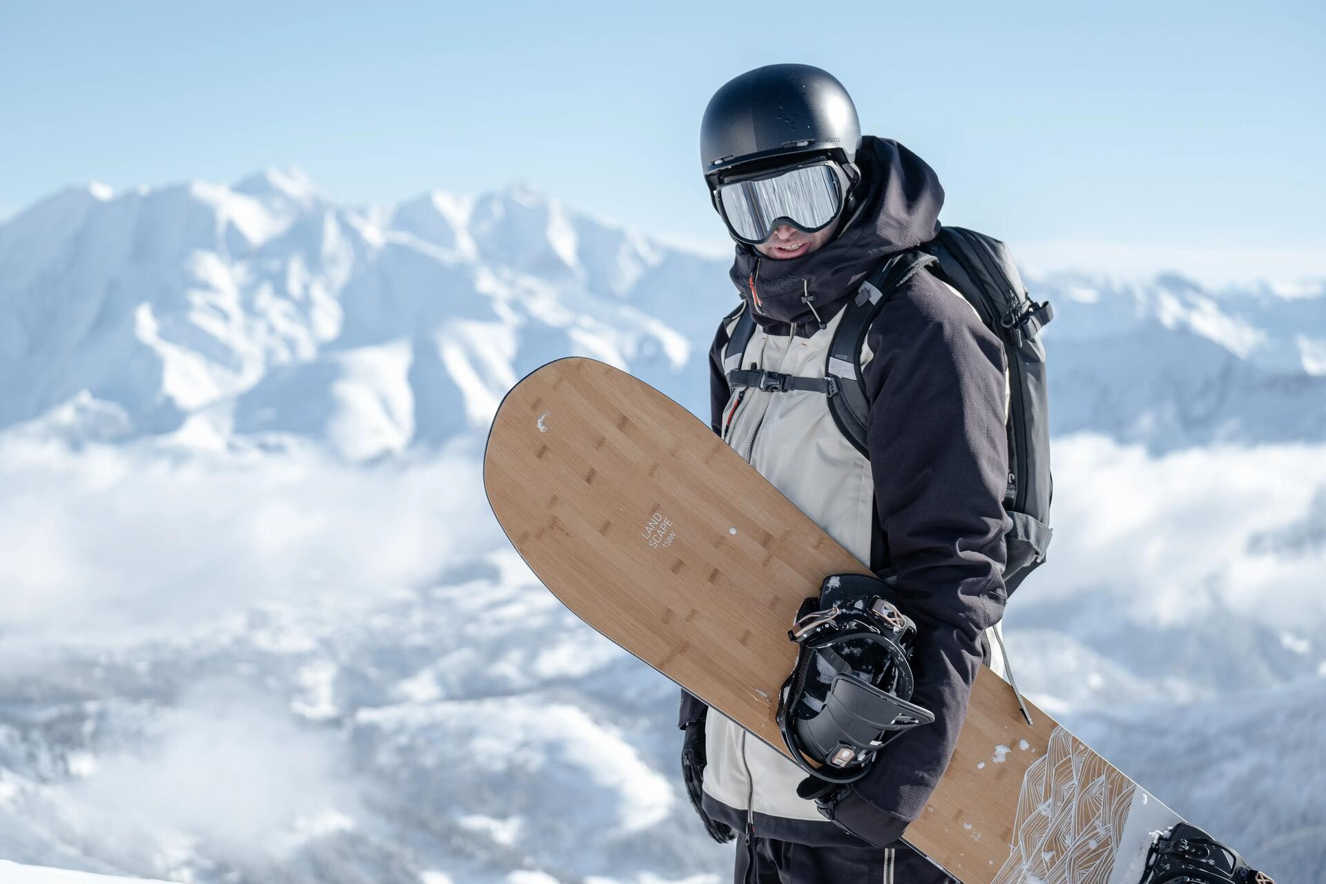 Mężczyzna w kasku i goglach snowboardowych trzymający deskę snowboardową w ręce