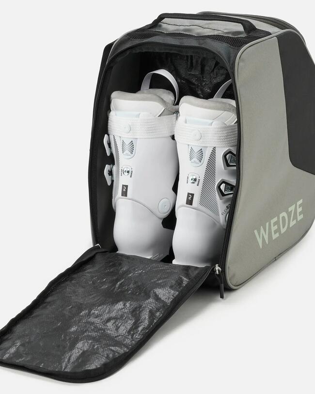 Geöffnete grau-schwarze Skischuhtasche mit weißen Skischuhen drin.