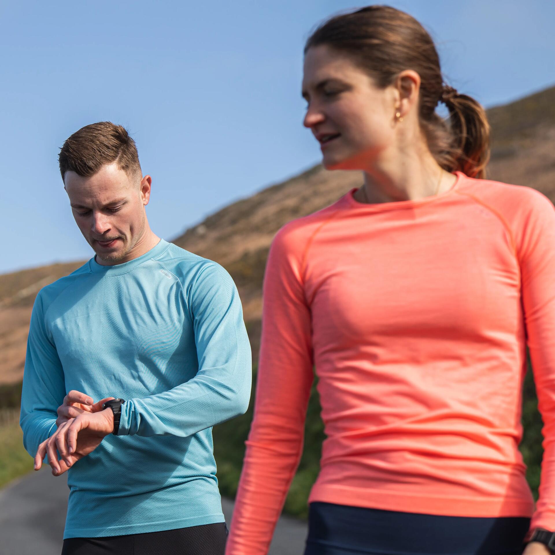 Zwei Jogger auf einer Landstraße, tragen bunte Sportkleidung in Blau und Orange, im Hintergrund Natur und sanfte Hügel.