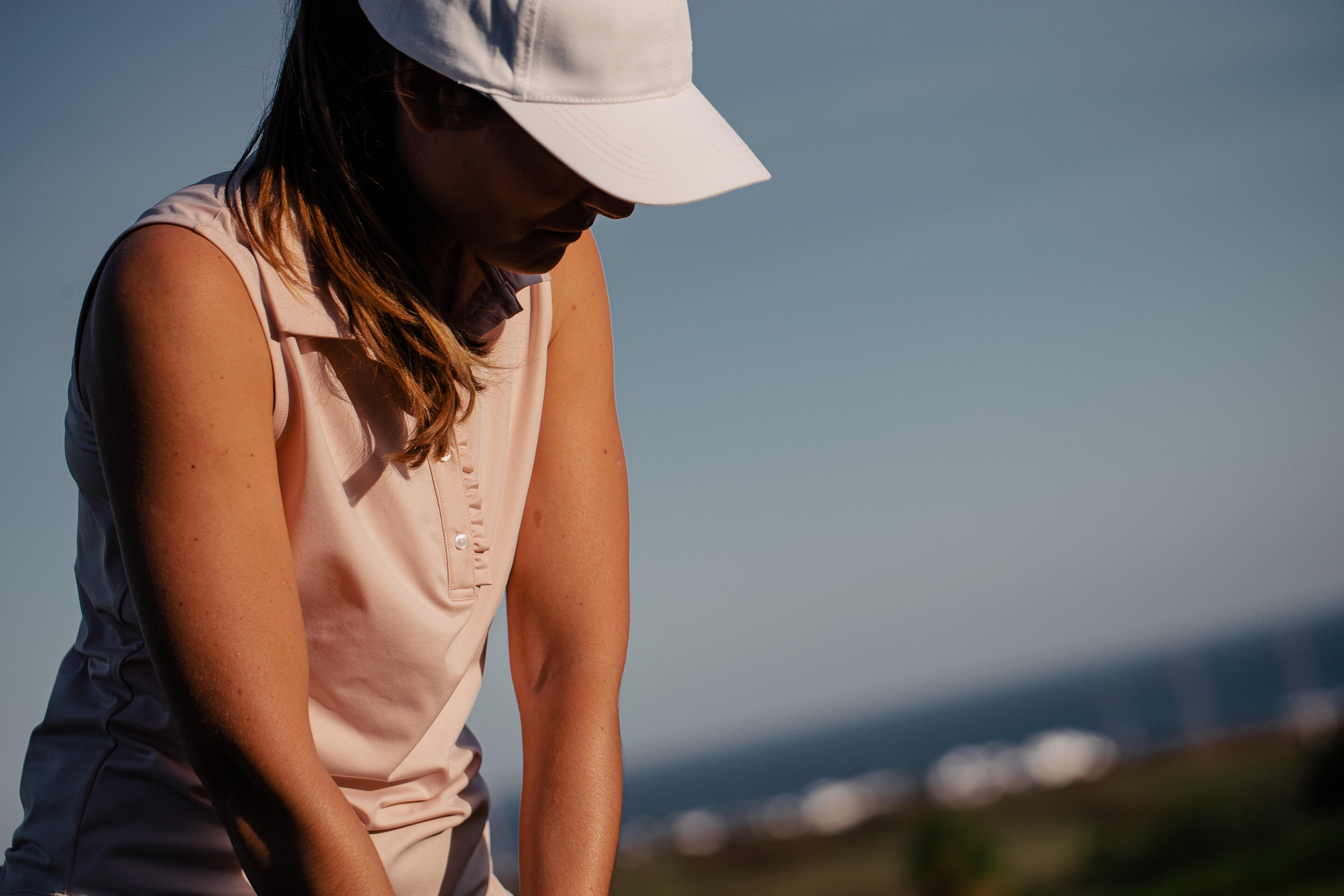 Pale pink sleeveless polo and white cap worn by a woman outdoors