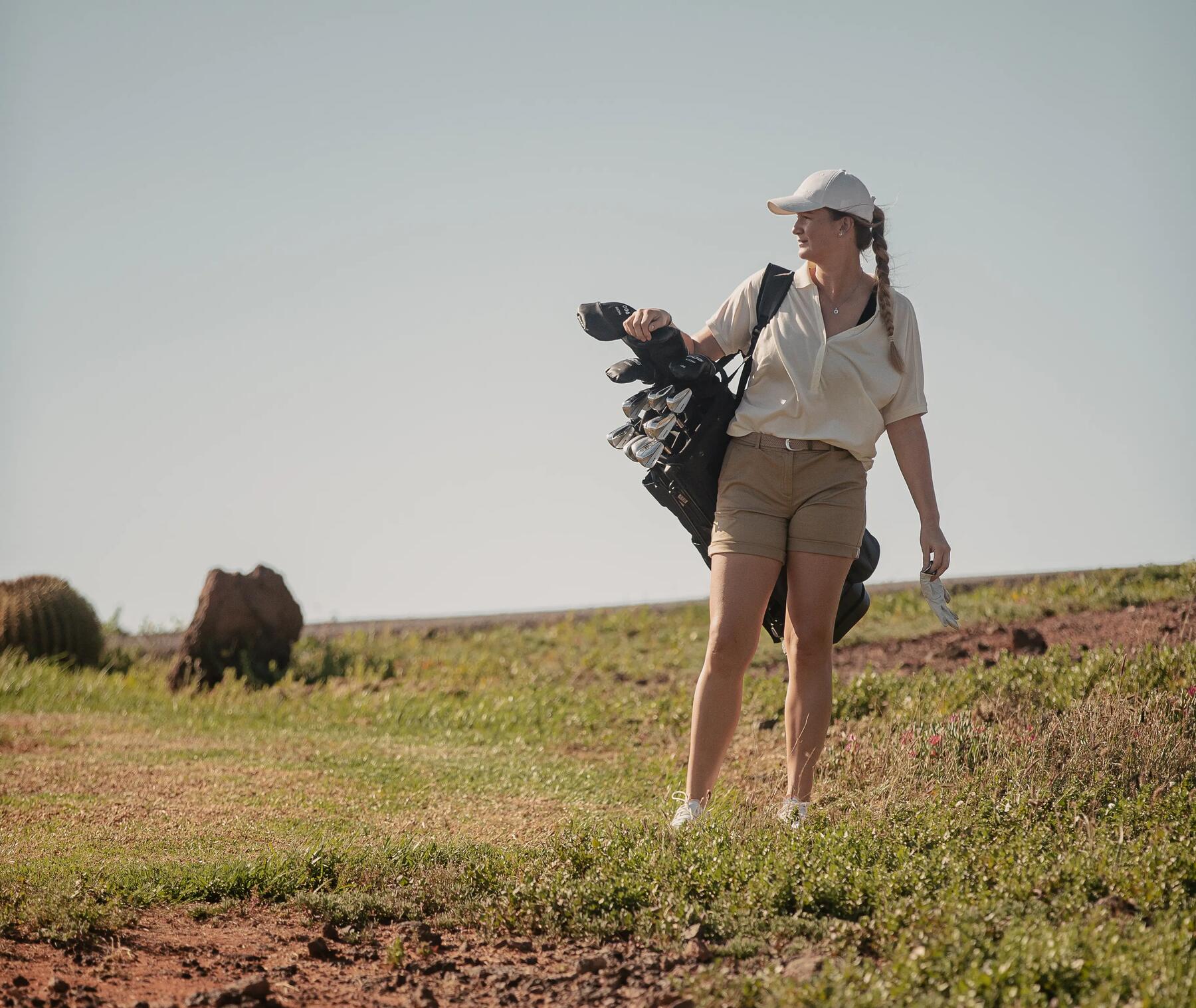 Frau steht mit Tasche und Golfbällen auf dem Platz