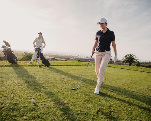 Kobieta ubrana w strój i buty do golfa trzymająca kij golfowy
