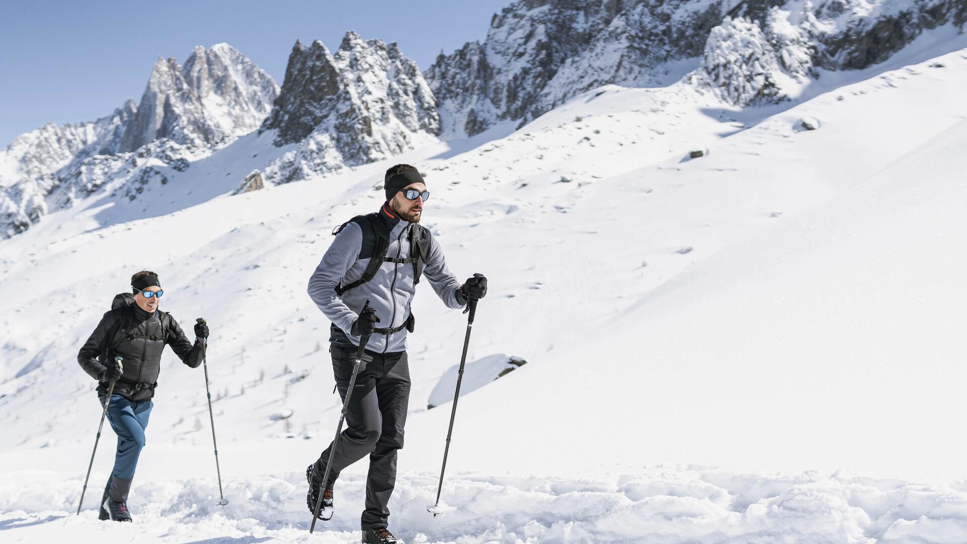 mężczyźni chodzący po górach w butach trekkingowych z kijami trekkingowymi w rękach