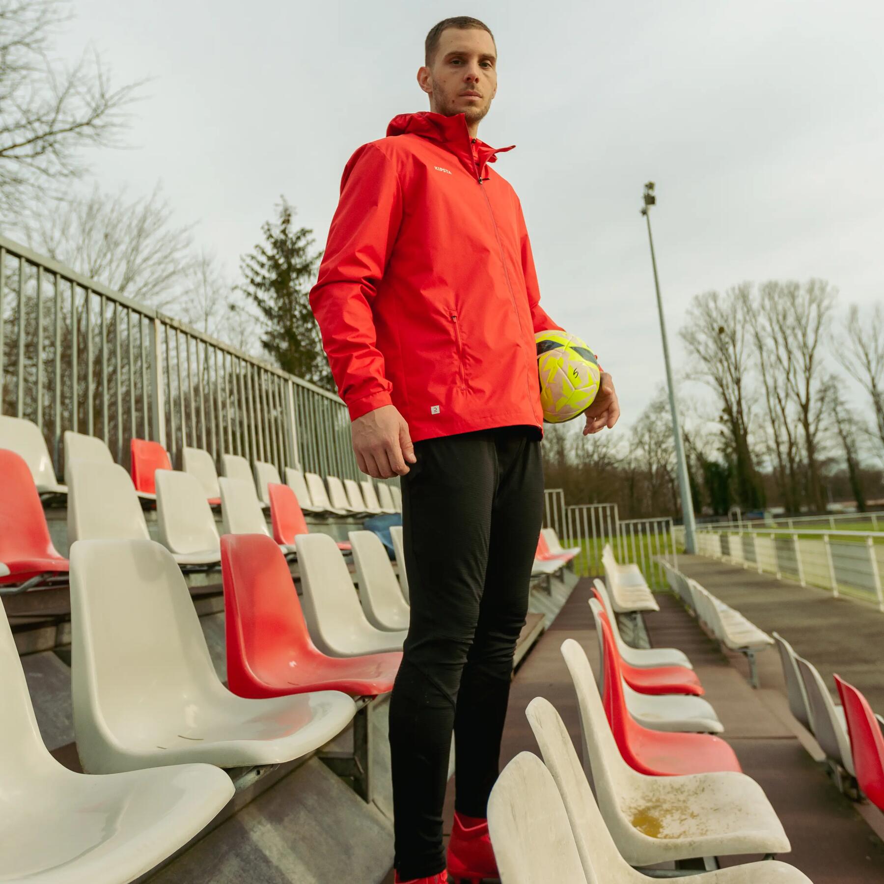 Trener piłki nożnej w odzieży sportowej stojący na trybunach boiska trzymając piłkę do piłki nożnej