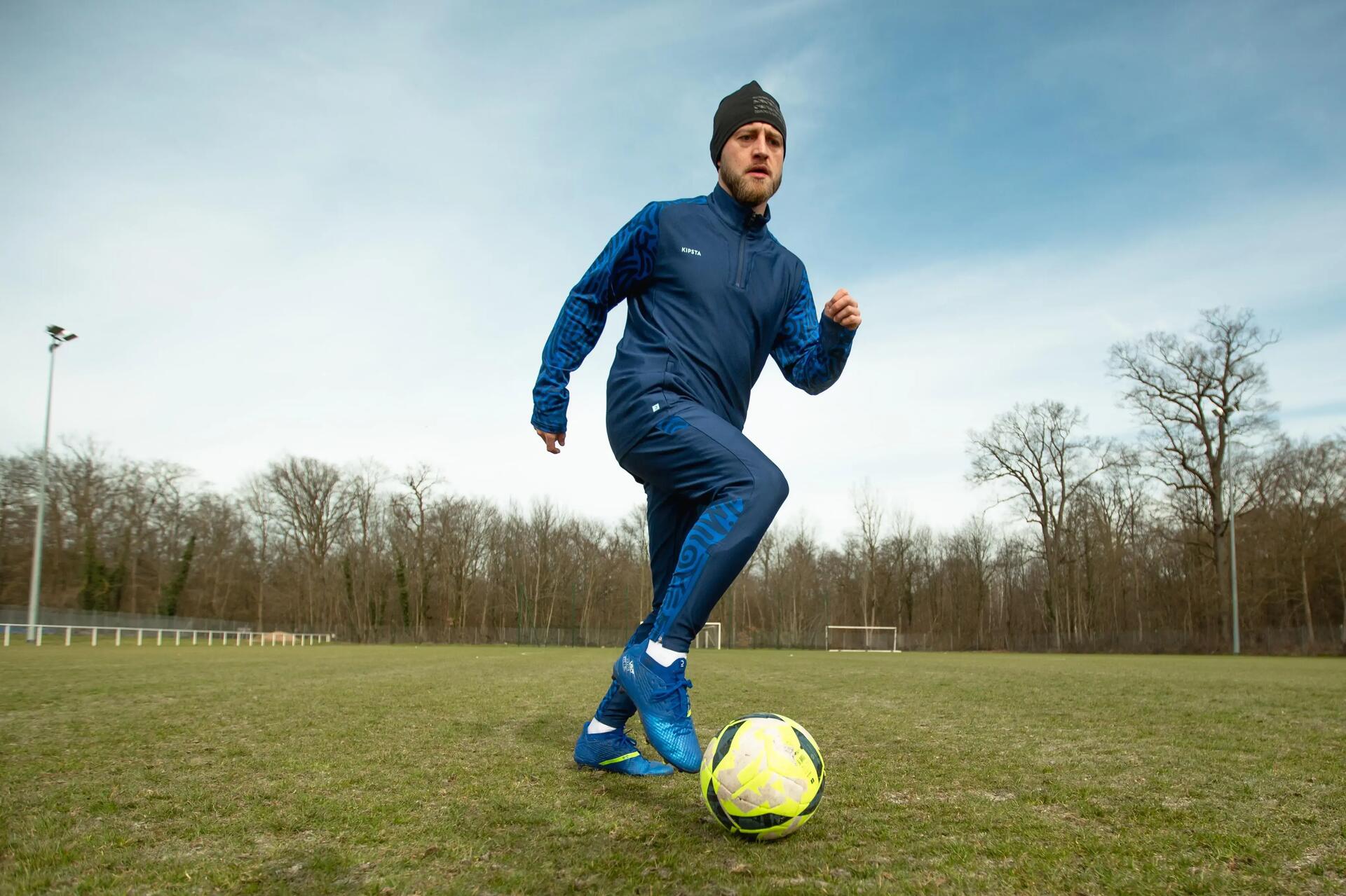piłkarz w czapce i ciepłej odzieży piłkarskie wykonujący trening piłkarski zimą na boisku