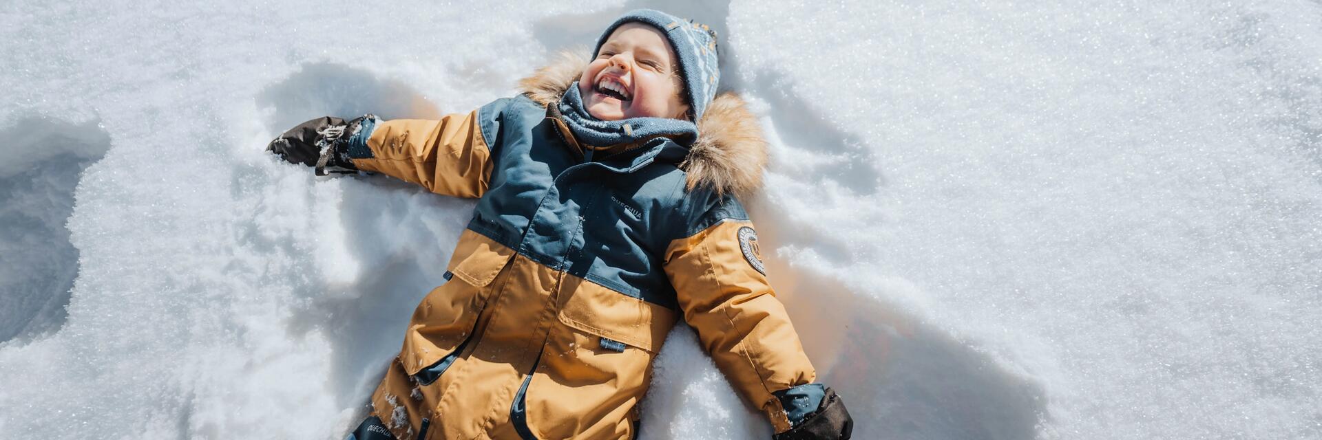Zadowolone dziecko z zabawy na śniegu robiące aniołka na śniegu