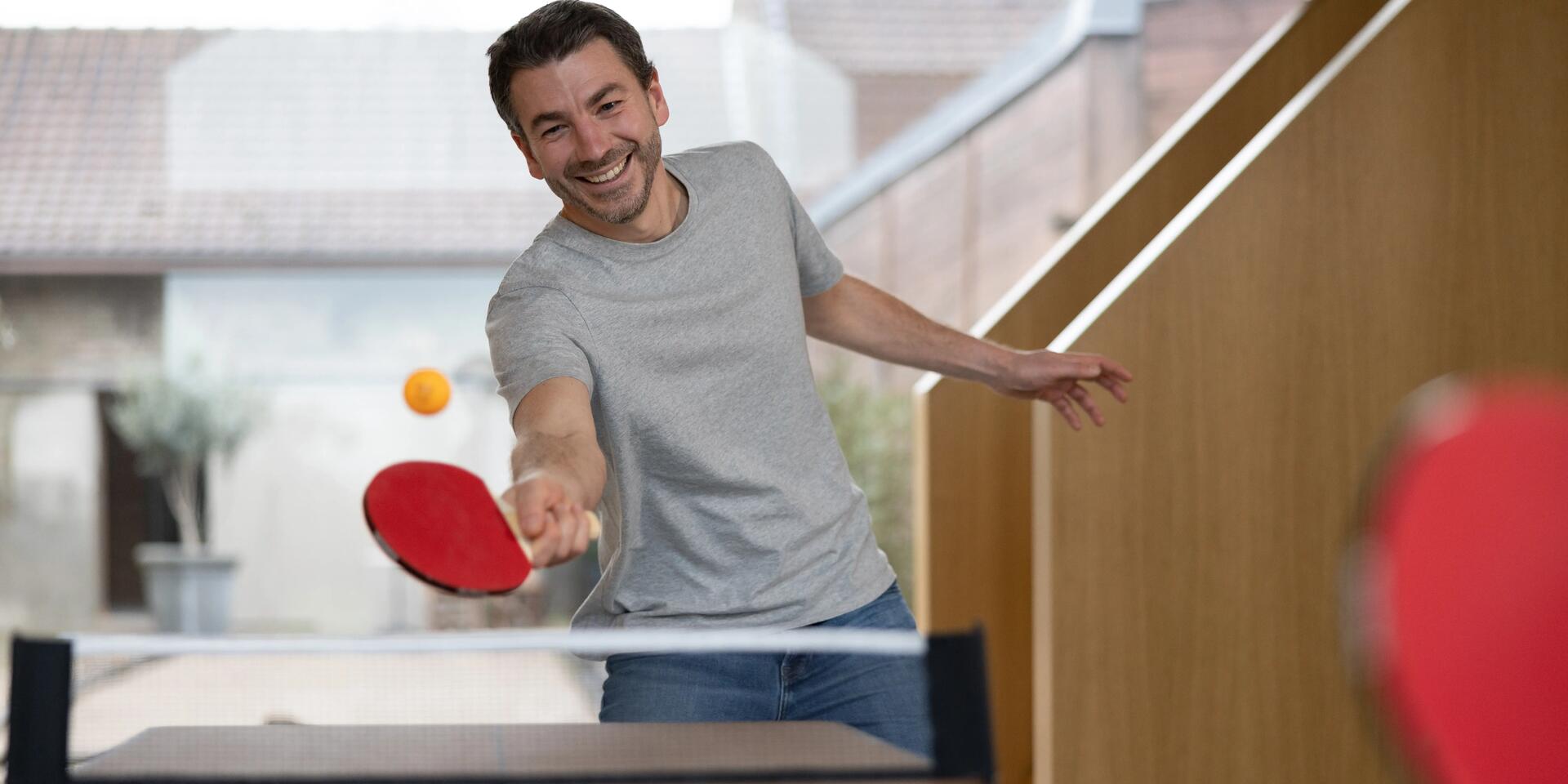 mężczyzna odbijający piłeczkę do ping-ponga trzymając rakietkę do tenisa stołowego w dłoni