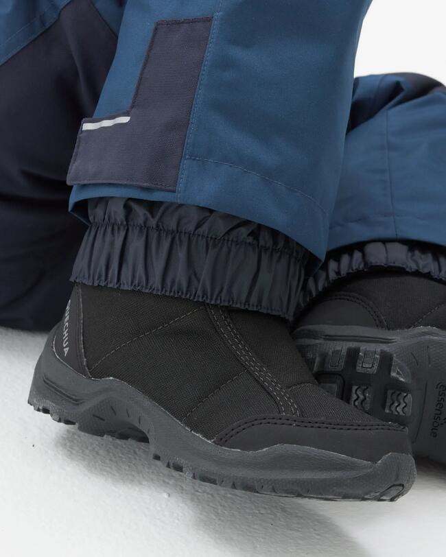 Beinabschluss der blauen Winterhose, der über die schwarzen Winterschuhe geht.