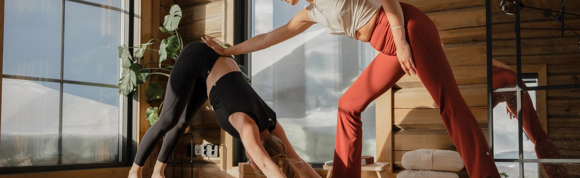 kobieta wykonująca asanę na macie do jogi  z pomocą instruktorki