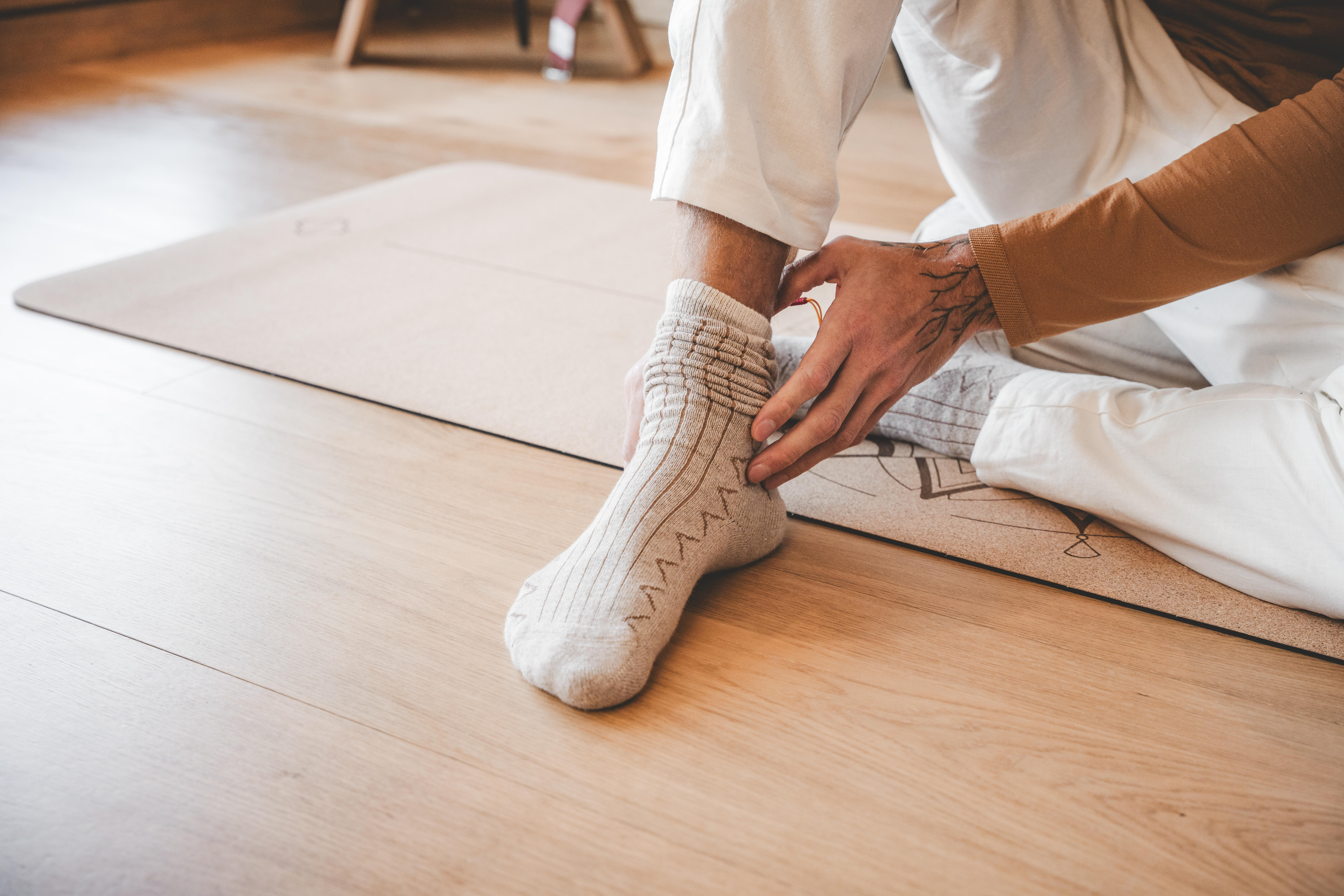 Person adjusting a thick beige sock while seated on a yoga mat