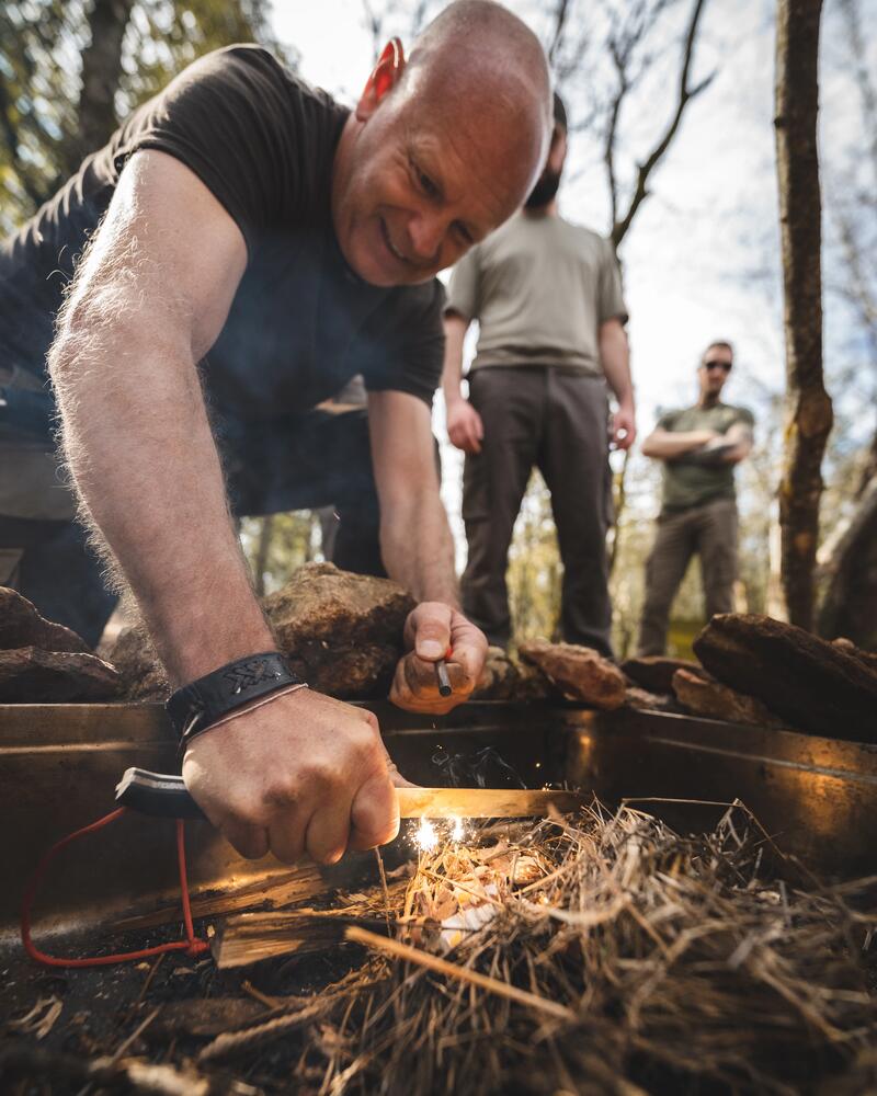Ein Mann versucht mit einem Feuerstahl ein Lagerfeuer zu entzünden