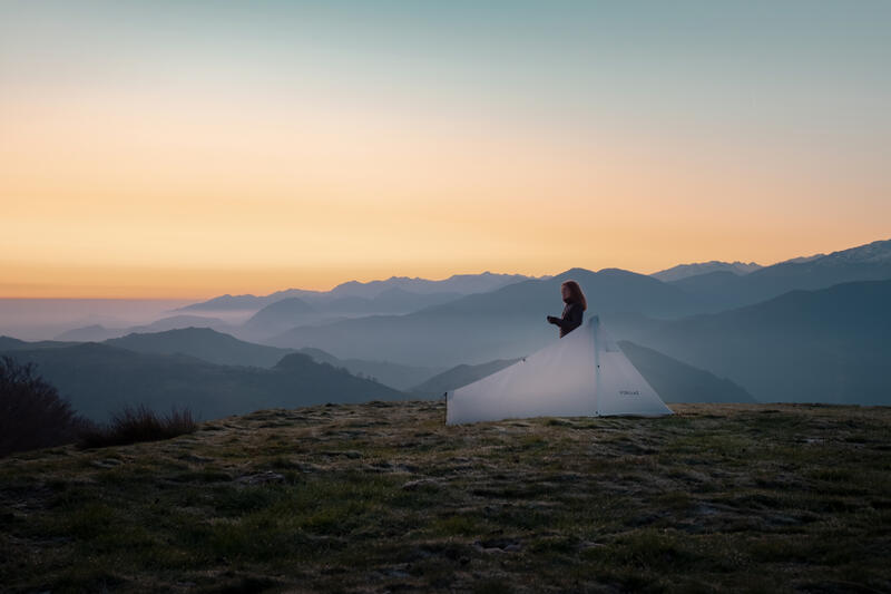 Kobieta stojąca obok namiotu dwuosobowego podziwiająca górski widok