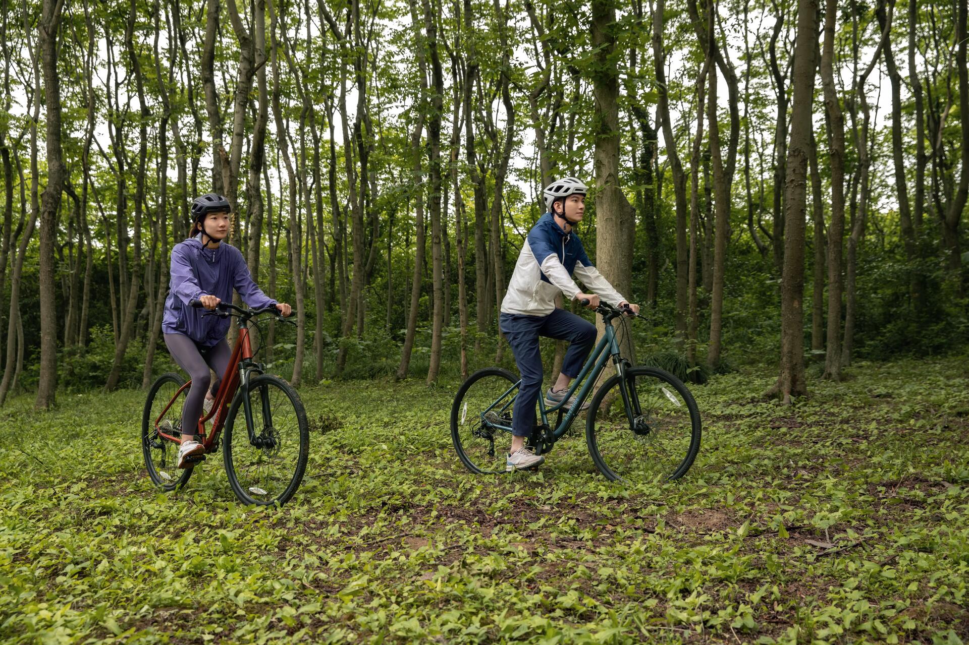 Kobieta i mężczyzna jadący na rowerach trekkingowych w kaskach po lesie