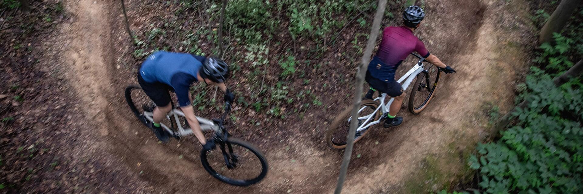 Rowerzyści w kaskach jadący rowerami po wąskiej ścieżce w lesie