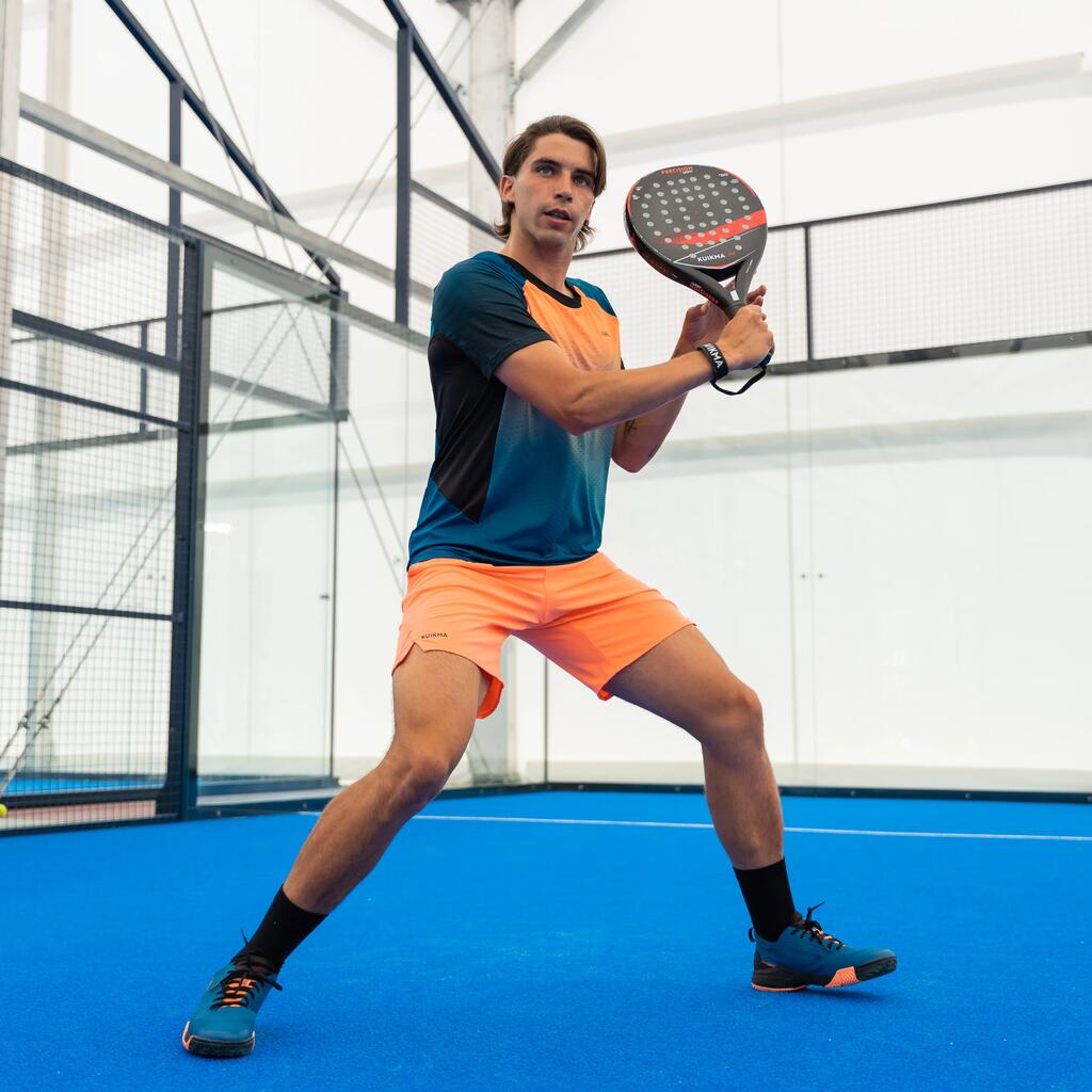 Ein Padelspieler auf einem Padelcourt, der eine orangefarbene Shorts trägt.