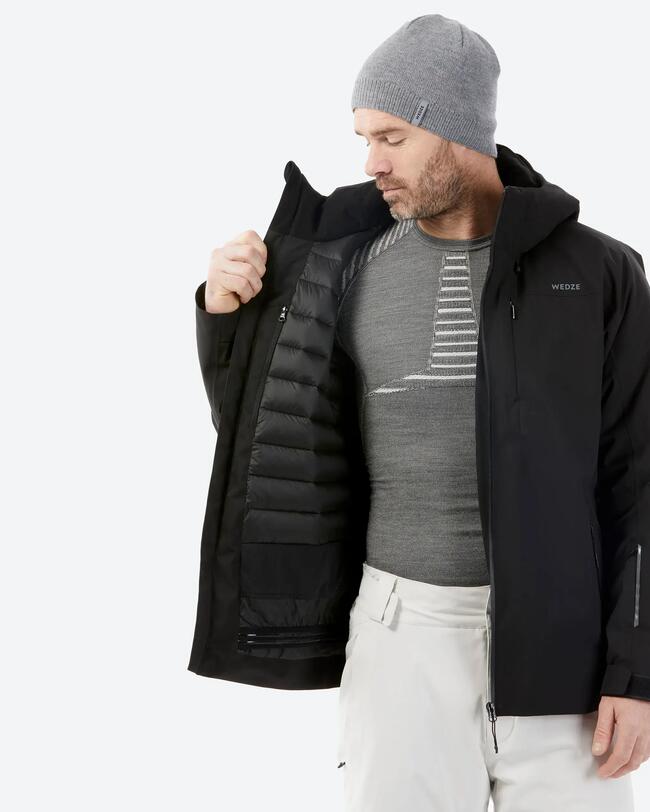 Ein Mann mit grauem Baselayer und einer grauen Beanie hat die schwarze Jacke an und zeigt die Innenseite.