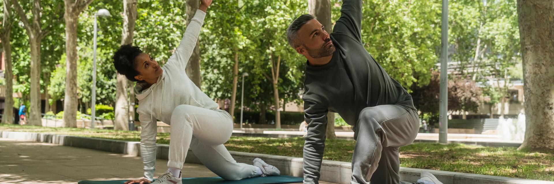 Kobieta i mężczyzna w odzieży sportowej wykonujący stretching na matach do ćwiczeń w plenerze