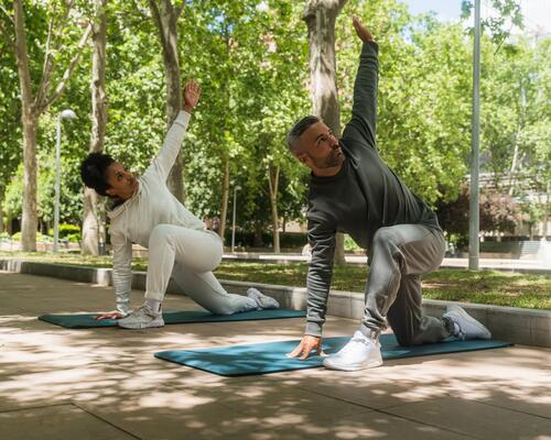 Kobieta i mężczyzna w odzieży sportowej wykonujący stretching na matach do ćwiczeń w plenerze