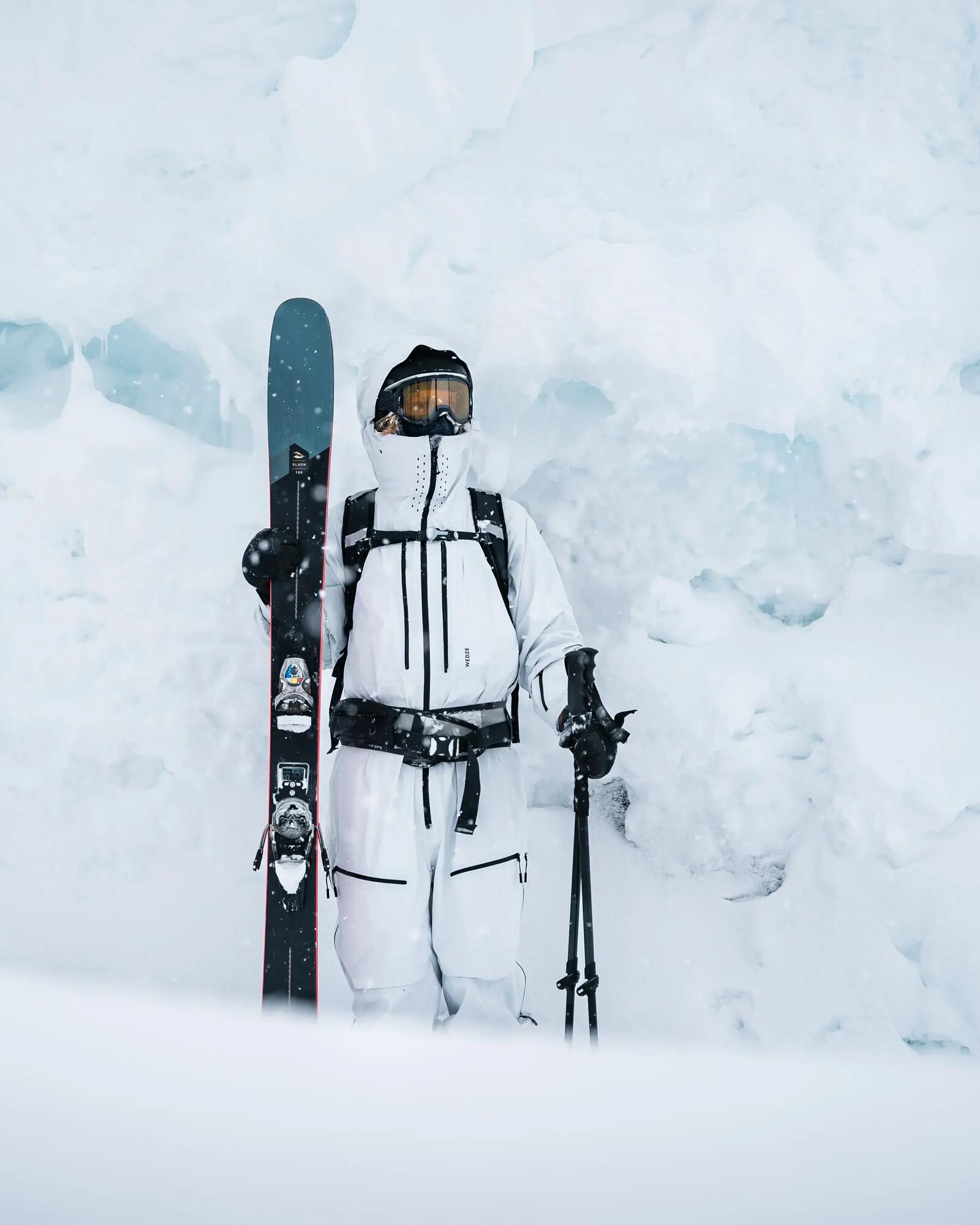 Eine Skifahrerin steht in weißer Bekleidung im Schnee und hat ihre Skier in der Hand.