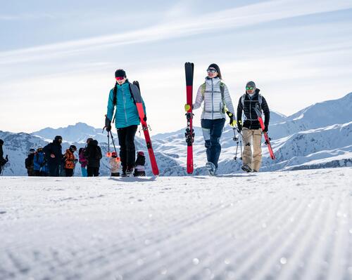 Narciarze idący na stoku trzymając kije narciarskie i narty dobrane do wzrostu 