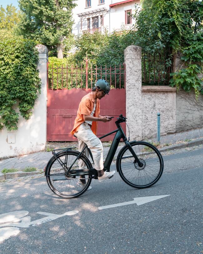 Mann auf Fahrrad, an einer Steigung stehend, schaut auf sein Handy