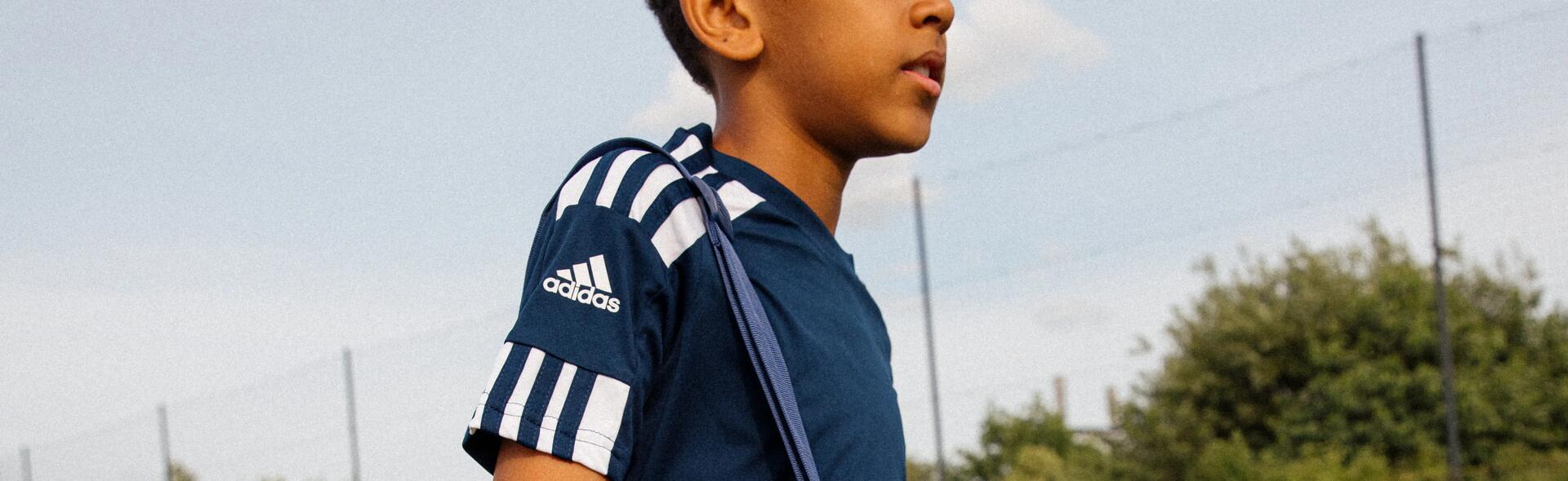 chłopiec idący po murawie zw stroju piłkarskim z torbą piłkarską na ramieniu