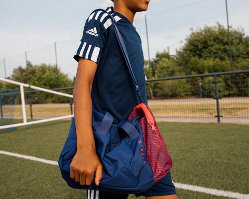 chłopiec idący po murawie zw stroju piłkarskim z torbą piłkarską na ramieniu
