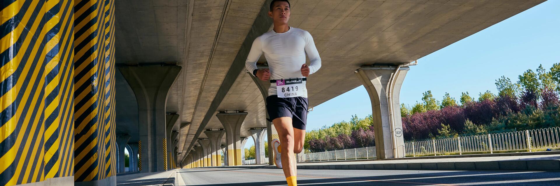 Mężczyzna w odzieży sportowej biegnący w maratonie po asfalcie pod mostem