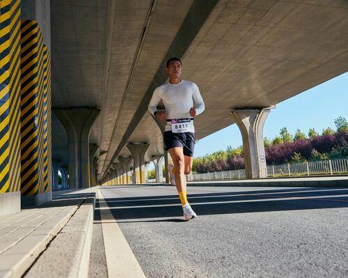 Mężczyzna w odzieży sportowej biegnący w maratonie po asfalcie pod mostem