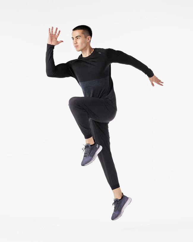 Mann in dunkler Sportkleidung springt dynamisch auf weißem Hintergrund, hebt linkes Knie an, Energie und Bewegung sichtbar
