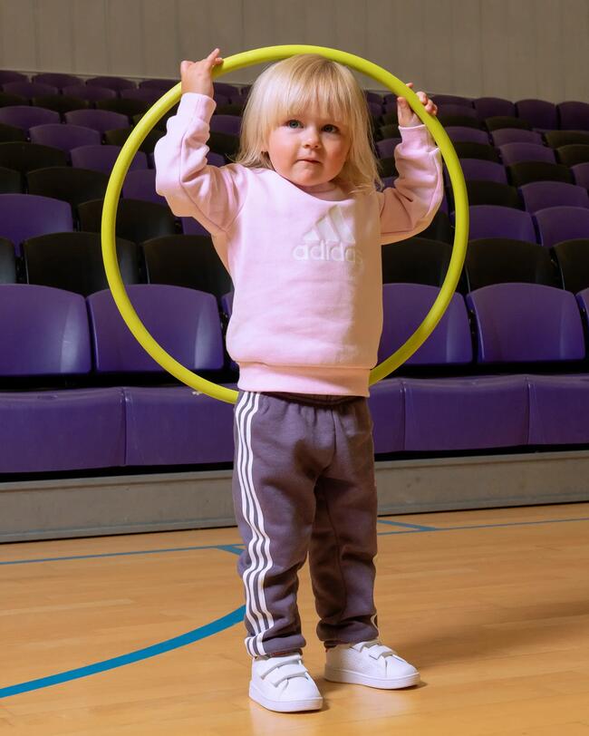 Mädchen in Adidas Trainingsanzug hält einen Hula Hoop in die Luft.