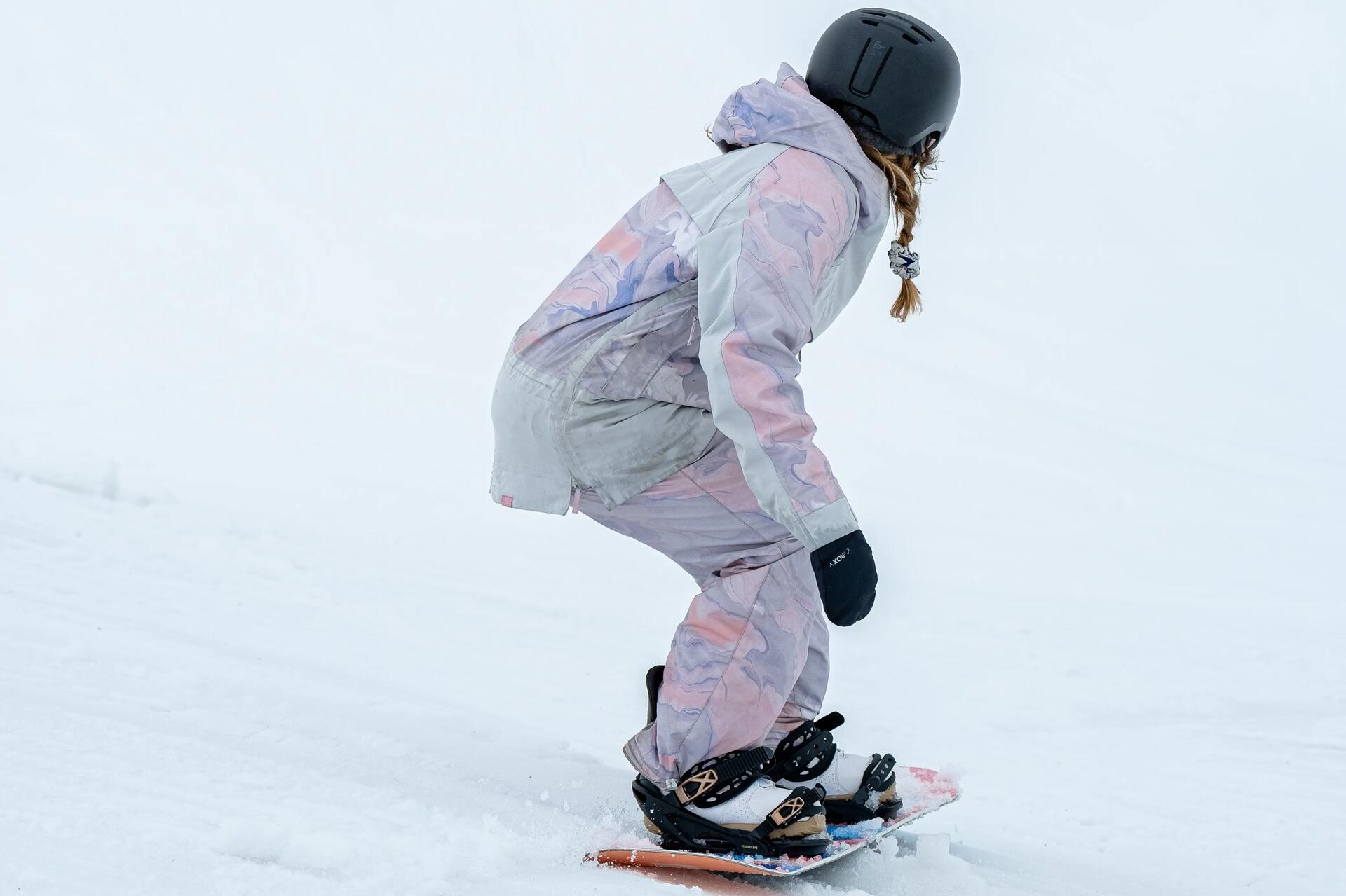 Kobieta w odzieży zimowej w kasku jeżdżąca na desce snowboardowej