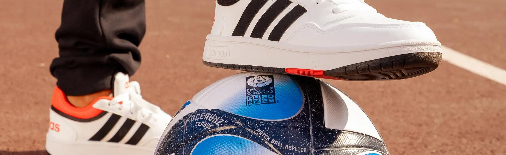 osoba w butach i spodniach firmy adidas trzymająca nogę na piłce do piłki nożnej